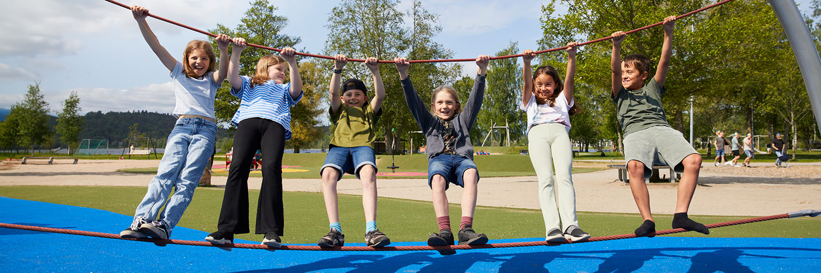 A group of children balance on a rope and hold onto another rope overhead, they are all facing the camera and smiling.